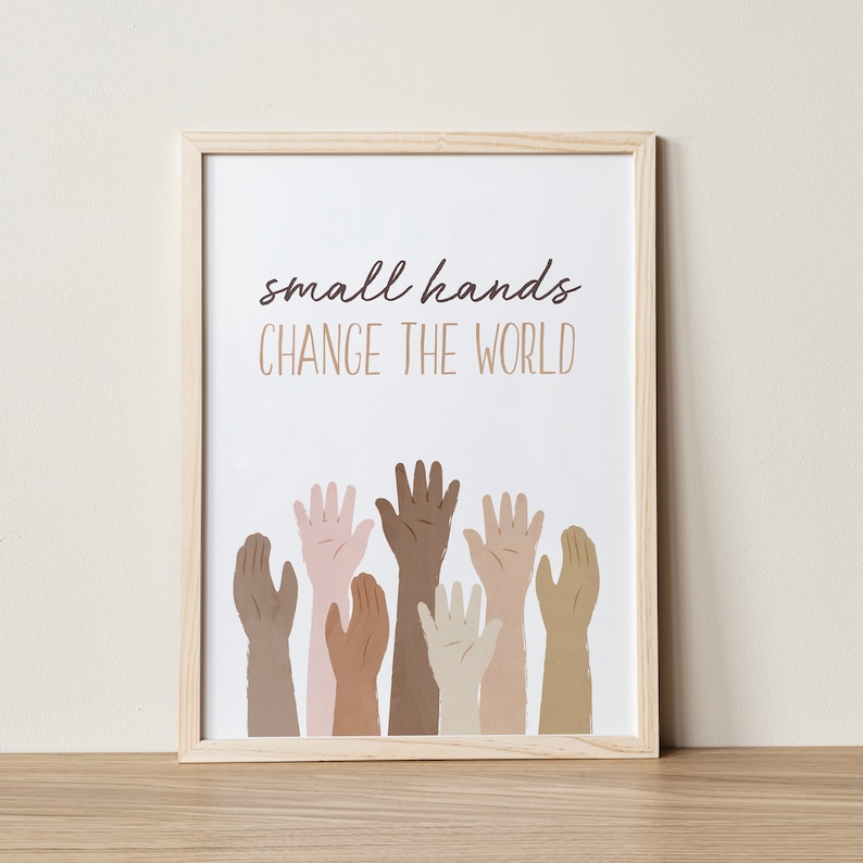 May include: A framed print with the text "small hands CHANGE THE WORLD" in brown lettering. The print features an illustration of multiple hands of different skin tones reaching up.