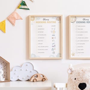May include: Two framed children's routine charts, one for morning and one for evening, with a light wood frame. The charts have a soft, pastel color scheme with illustrations. A wooden car, cloud-shaped light, and bear-shaped pillow are on a white shelf.