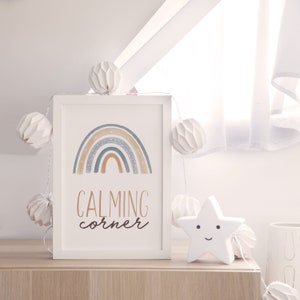 May include: A white framed print with a watercolor rainbow and the text "CALMING corner". The print is on a wooden surface with white paper lanterns and a white star-shaped nightlight.
