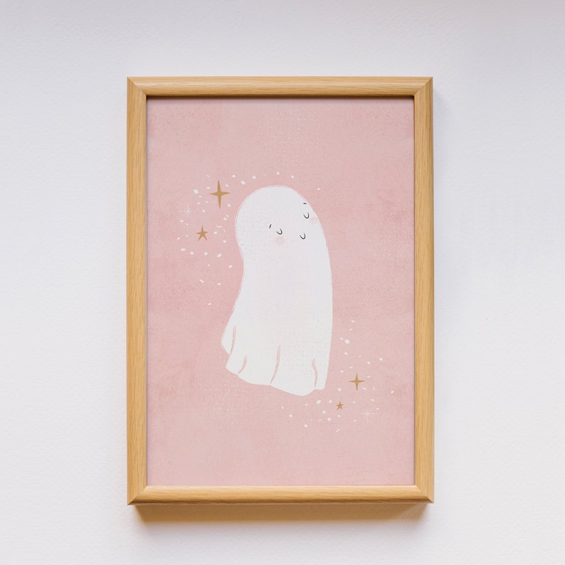 May include: A framed print with a pink background and a white ghost with a cute face. The ghost is surrounded by gold glitter stars.
