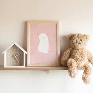 May include: A white wooden house-shaped clock with black hands and a pink and white framed print of a ghost with gold stars on a pink background. A brown teddy bear sits on a wooden shelf.