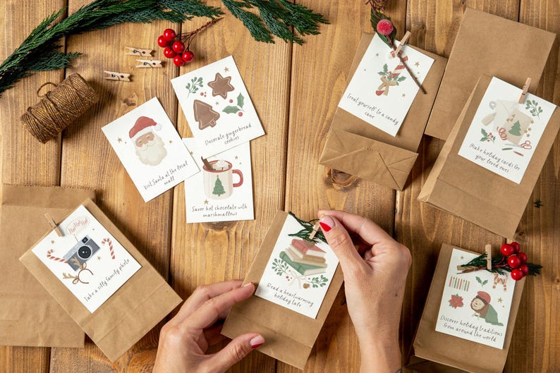 May include: A flat lay of brown paper gift bags with festive Christmas gift tags attached. The tags feature illustrations of Santa Claus, gingerbread cookies, hot chocolate, a camera, books, and a winter scene. The tags have text that reads "Find yourself a candy cane", "Hot cocoa and marshmallows", "Have a silly family photo", "Read a heartwarming holiday tale", "Discover holiday traditions from around the world", and "Best wishes of the season".