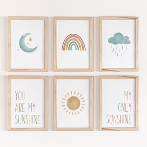 Puede incluir: Seis impresiones enmarcadas con un tema de acuarela. Las impresiones presentan una luna creciente, un arcoíris, una nube con gotas de lluvia, un sol y dos impresiones de texto que dicen "You are my sunshine" y "My only sunshine".