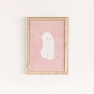 May include: A framed print of a white ghost with a pink background and gold glitter. The ghost has a cute, friendly expression.