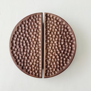 May include: Two-piece, semi-circular wooden cabinet pulls with a textured, hammered surface. The pulls are a warm brown colour and are designed to be mounted on a cabinet door. The hardware is made of wood.