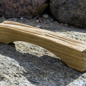 Könnte beinhalten: Ein Holzgriff mit einer gebogenen Form, aus Naturholz mit rustikalem Finish. Der Griff ist hellbraun und hat eine raue Textur.