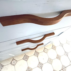 May include: A handmade, wooden serving tray with a natural finish. The tray features a rectangular shape with raised edges and integrated handles. The wood grain is visible, showcasing the tray's craftsmanship. Dimensions: 18 inches long, 12 inches wide, and 2 inches high.