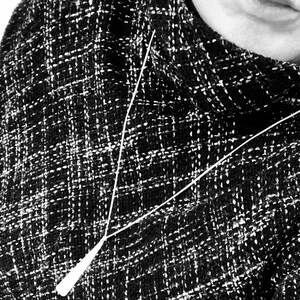 May include: Black and white tweed fabric with a white pendant necklace. The necklace has a long, thin chain and a teardrop-shaped pendant. The tweed fabric has a woven pattern.