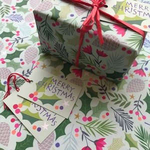 May include: A gift wrapped in green and white wrapping paper with a festive Christmas design. The paper features holly leaves, pine branches, berries, and pine cones. The gift is tied with a red ribbon and has two gift tags that say "Merry Christmas".