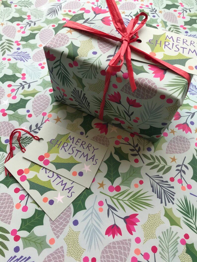 May include: A gift wrapped in green and white wrapping paper with a festive Christmas design. The paper features holly leaves, pine branches, berries, and pine cones. The gift is tied with a red ribbon and has two gift tags that say "Merry Christmas".