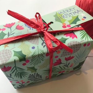 May include: A green gift box with a red ribbon and a gift tag that says "Merry Christmas". The box is wrapped in paper with a pattern of green leaves, red flowers, and white dots.