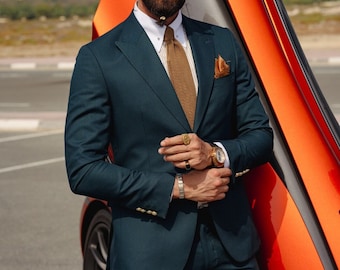 May include: A man wearing a dark green suit with a brown patterned tie and a white shirt. He is wearing sunglasses and a gold ring on his finger. He is standing next to a bright orange car.