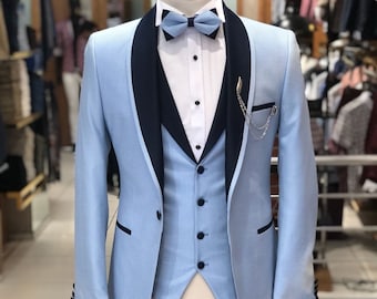 May include: A light blue suit with a black shawl collar, a white shirt, a bow tie, and a vest. The suit has a patterned design and a chain attached to the lapel.