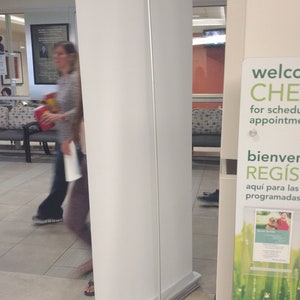 May include: A white retractable banner stand with a green and white sign that says "Welcome to CHE for scheduled appointments. Bienvenidos a REGIS aqui para las programadas. VISA CREDIT/DEBIT PAYMENT PAGO DE CR&Eacute;DITO/DEBIT".