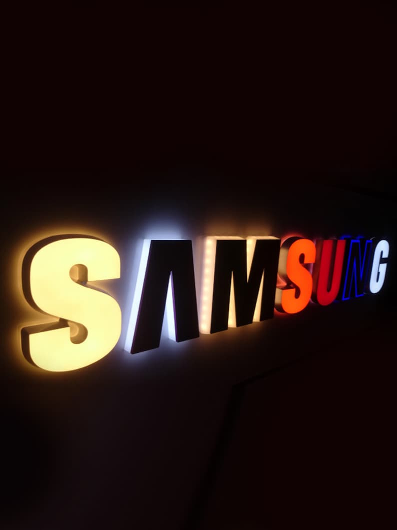 May include: A white, black, red, and blue illuminated sign that reads "SAMSUNG".