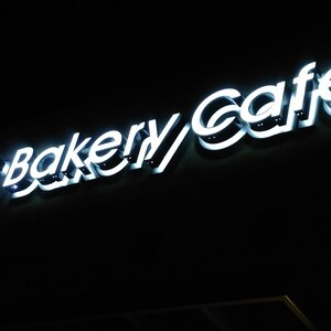 May include: A white neon sign with the text "85&deg;C Bakery Cafe" on a black background.