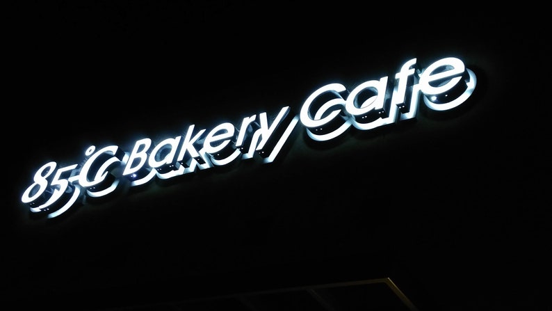 May include: A white neon sign with the text "85&deg;C Bakery Cafe" on a black background.
