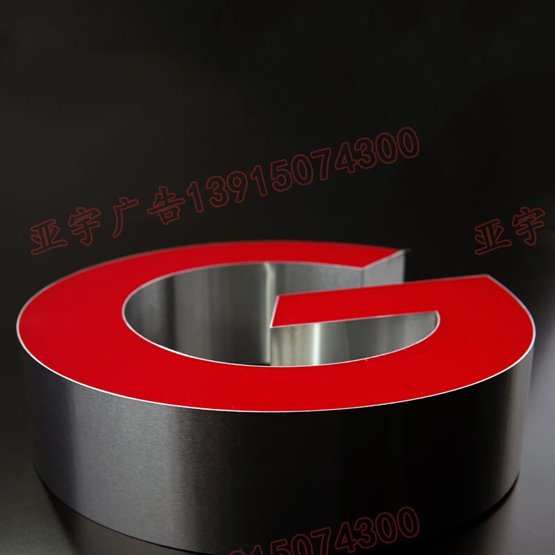 May include: A red and silver 3D letter G. The letter is made of metal and has a red acrylic face. The letter is sitting on a black surface.