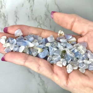 May include: A handful of small, tumbled blue and white gemstones. The stones vary in size and shape, with a mix of opaque and translucent qualities. The gemstones are a light blue color, with some having white or clear inclusions.