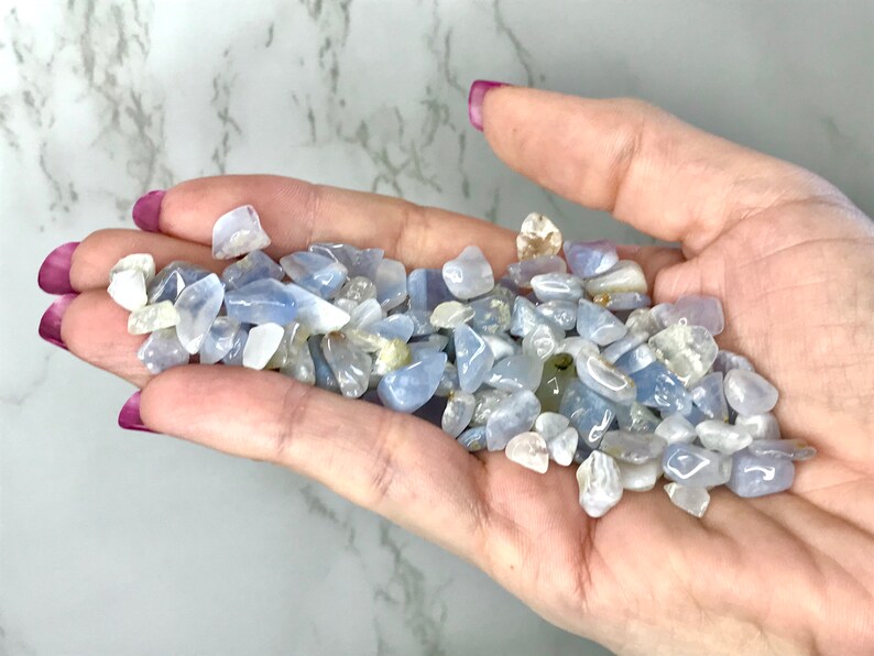 May include: A handful of small, tumbled blue and white gemstones. The stones vary in size and shape, with a mix of opaque and translucent qualities. The gemstones are a light blue color, with some having white or clear inclusions.