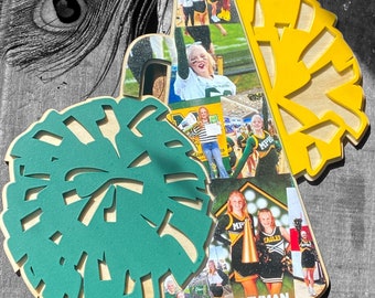 May include: A wooden cheerleader megaphone with a collage of photos of cheerleaders in green and gold uniforms. The megaphone is decorated with a green and gold pom-pom and the text "GEYMAN 2023".