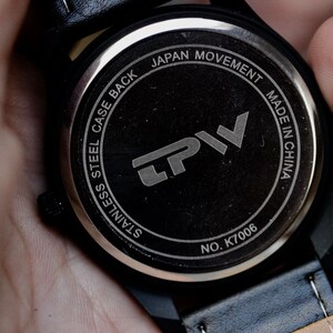 May include: Close-up of the back of a black wristwatch. The watch face is black with silver text that reads "STAINLESS STEEL CASE BACK JAPAN MOVEMENT MADE IN CHINA" and the brand logo "LPV". The model number is K7006.