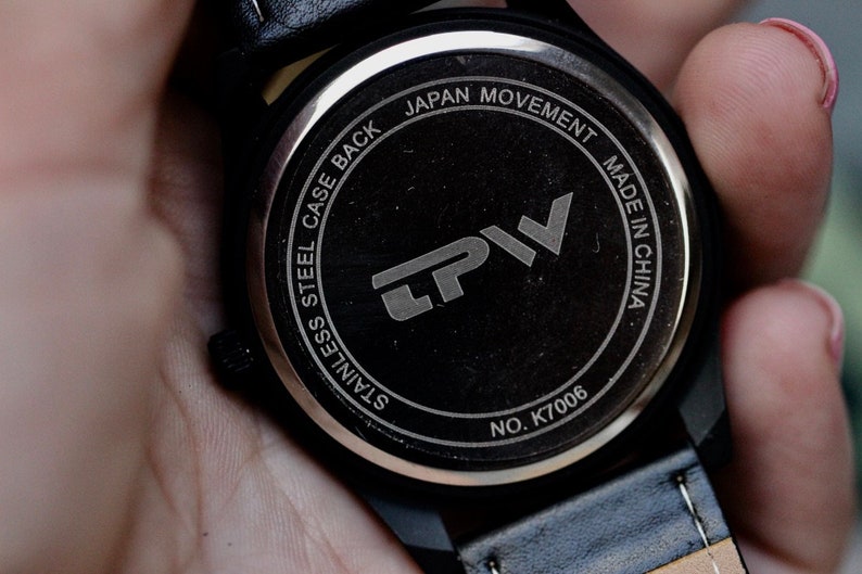 May include: Close-up of the back of a black wristwatch. The watch face is black with silver text that reads "STAINLESS STEEL CASE BACK JAPAN MOVEMENT MADE IN CHINA" and the brand logo "LPV". The model number is K7006.
