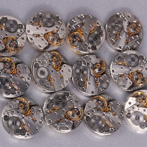 May include: Twelve silver and gold watch movements with intricate gears and mechanisms.