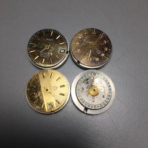 Puede incluir: Cuatro esferas de reloj vintage en tonos dorados y plateados. Dos esferas muestran el n&uacute;mero 25. La palabra "buch" es visible en una. Las esferas muestran signos de desgaste, con ara&ntilde;azos y decoloraci&oacute;n visibles.