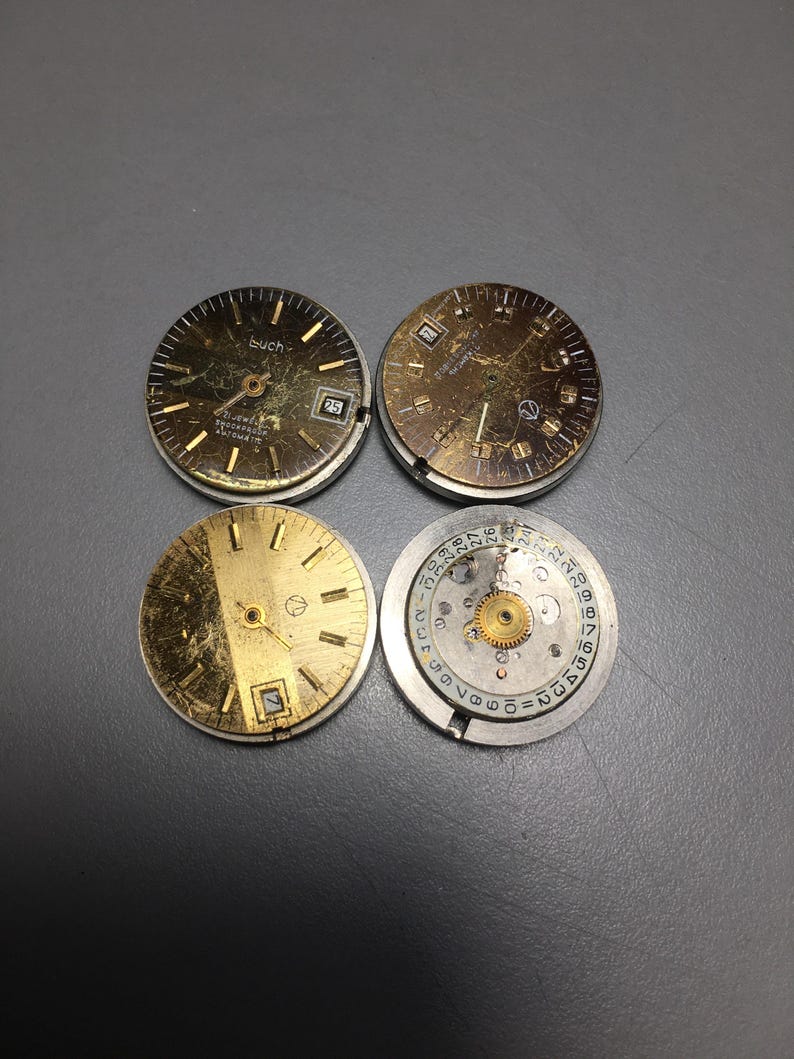 Puede incluir: Cuatro esferas de reloj vintage en tonos dorados y plateados. Dos esferas muestran el n&uacute;mero 25. La palabra "buch" es visible en una. Las esferas muestran signos de desgaste, con ara&ntilde;azos y decoloraci&oacute;n visibles.