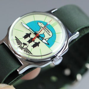May include: A vintage wristwatch with a green leather band. The watch face features a white background with a green and blue design of a polar bear and penguins. The text "СССР" is printed on the watch face.