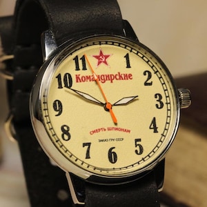 May include: A vintage wristwatch with a cream-colored face, black numerals, and red text. The watch features a red star and an orange second hand. It has a black leather strap and a silver-colored case.