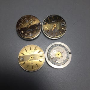 Puede incluir: Cuatro esferas de reloj vintage. Dos tienen esferas doradas y negras con manecillas y n&uacute;meros, una con ventana de fecha. La cuarta muestra el mecanismo interno con engranajes y n&uacute;meros. Las esferas son circulares.