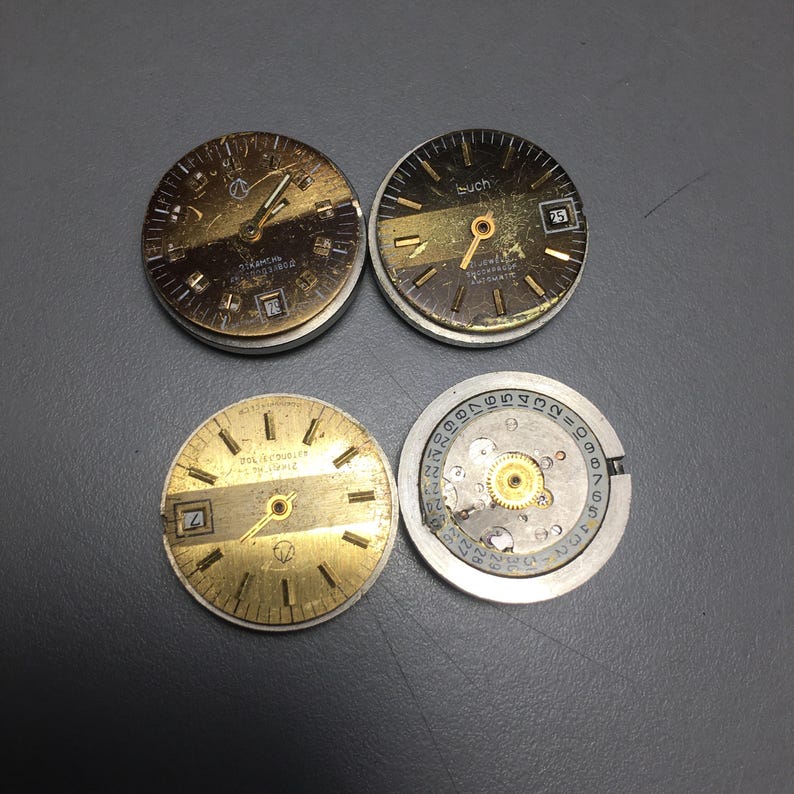Puede incluir: Cuatro esferas de reloj vintage. Dos tienen esferas doradas y negras con manecillas y n&uacute;meros, una con ventana de fecha. La cuarta muestra el mecanismo interno con engranajes y n&uacute;meros. Las esferas son circulares.