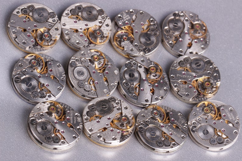 May include: A collection of 13 silver and gold watch movements with intricate gears and details.