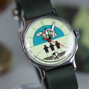 May include: A vintage wristwatch with a white face and a green strap. The watch face features a polar bear and penguins with the text "В.С.С.Р. СССР" in red.