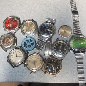 以下が含まれることがあります： さまざまな文字盤デザインと金属バンドを備えた、ヴィンテージの腕時計のコレクション。 赤、緑、黒など、さまざまな色の文字盤があり、数字と針が見えます。 バンドがない時計や、部品が外れている時計もあります。