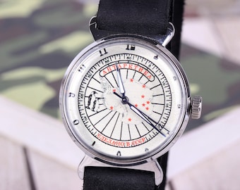 Puede incluir: Un reloj de pulsera analógico plateado con correa de cuero negro. La esfera color crema presenta un mapa de la Antártida con estrellas rojas, una ilustración de un pingüino y el texto cirílico "АНТАРКТИКА" y "СДЕЛАНО В СССР" en rojo.