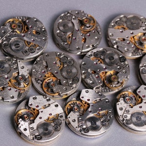 May include: Close-up of twelve silver and gold watch movements with intricate gears and mechanisms.