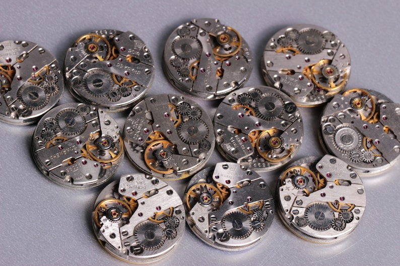 May include: Close-up of twelve silver and gold watch movements with intricate gears and mechanisms.
