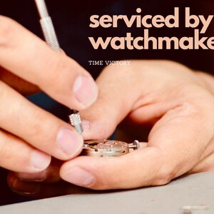 May include: A watchmaker is shown servicing a watch. The image includes the text "serviced by a watchmaker" and "TIME VICTORY". The watch is being worked on with a small tool.
