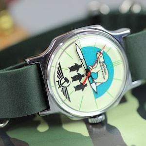 May include: A green leather wristband with a silver watch face featuring a polar bear and penguins on a blue and white background. The watch face also has the text "3 БАЙКАЛ" in Cyrillic script.