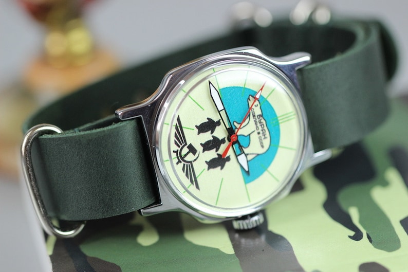 May include: A green leather wristband with a silver watch face featuring a polar bear and penguins on a blue and white background. The watch face also has the text "3 БАЙКАЛ" in Cyrillic script.