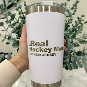 以下が含まれることがあります： 「the Real Hockey Moms of New Jersey」という金色の文字が書かれた白いステンレス製のタンブラーです。
