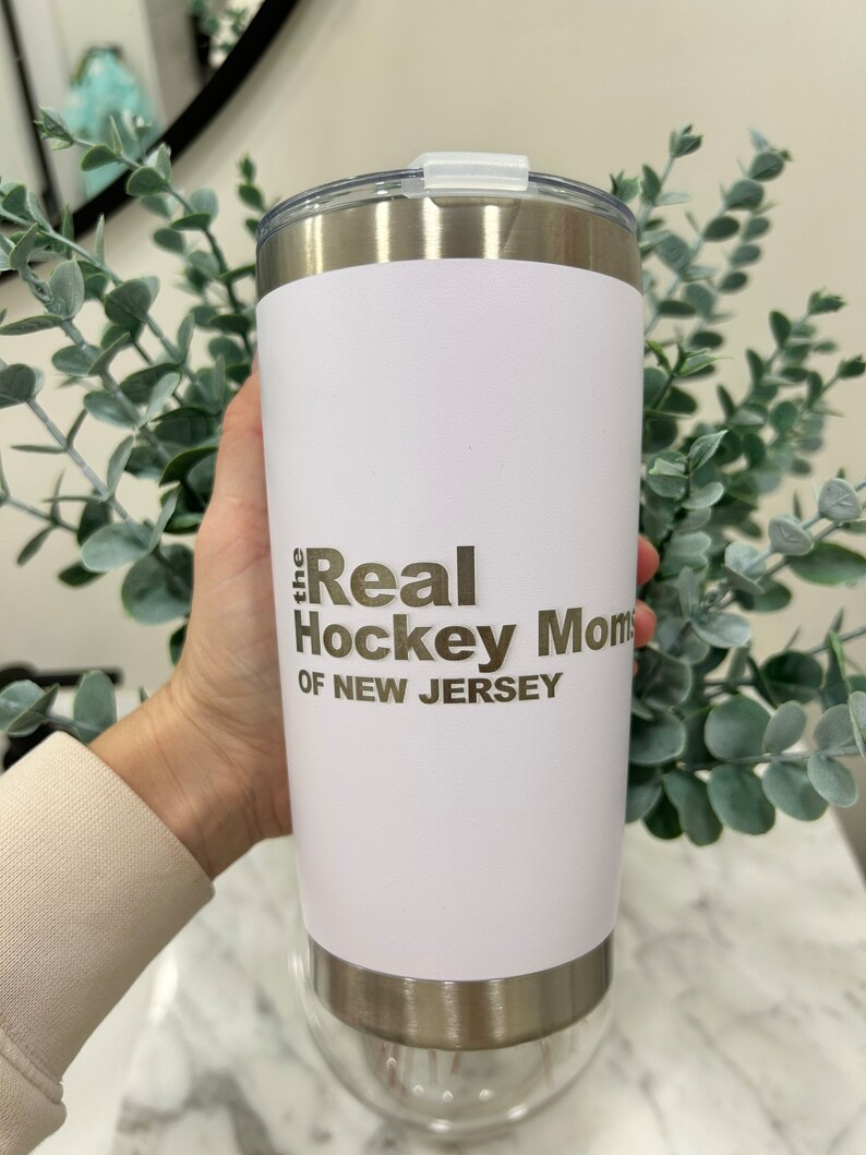 以下が含まれることがあります： 「the Real Hockey Moms of New Jersey」という金色の文字が書かれた白いステンレス製のタンブラーです。