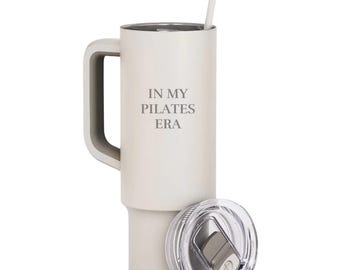 May include: White stainless steel travel mug with a handle and a lid. The mug has the text "IN MY PILATES ERA" printed on the side.