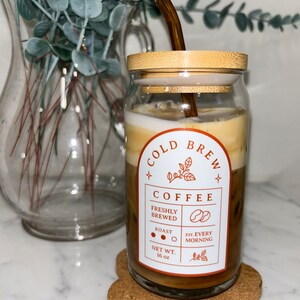 May include: A glass jar with a bamboo lid filled with cold brew coffee. The jar has a label that says "Cold Brew Coffee" with the text "Freshly Brewed", "Roast", "Est. Every Morning", and "Net Wt. 16 oz". A brown glass straw is in the jar.