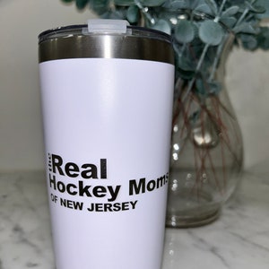 以下が含まれることがあります： 「The Real Hockey Moms of New Jersey」という黒いグラフィックが描かれた白いステンレス製のタンブラーです。