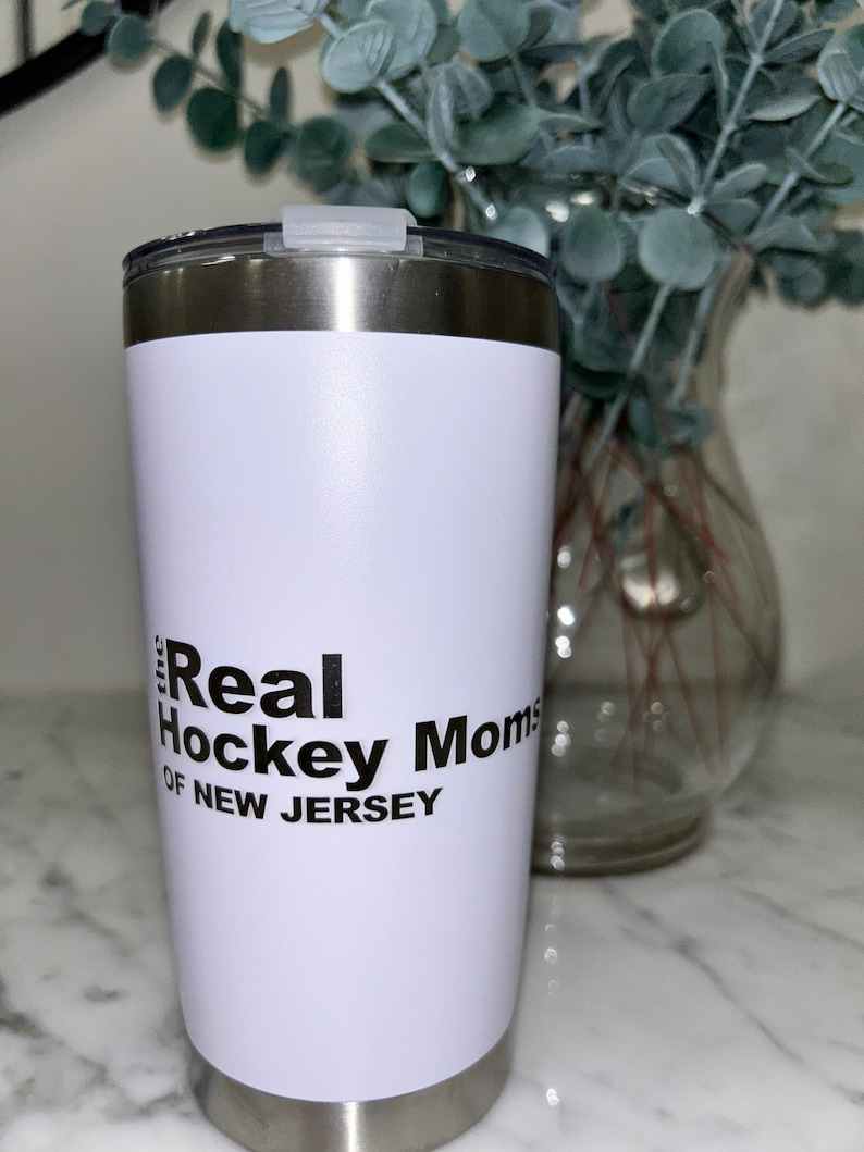 以下が含まれることがあります： 「The Real Hockey Moms of New Jersey」という黒いグラフィックが描かれた白いステンレス製のタンブラーです。