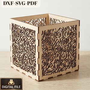 May include: A square wooden box with intricate floral cutouts. The box is made of light-colored wood and features a detailed, swirling pattern. The top of the box is open, and the sides are adorned with the decorative design. The words "DXF-SVG-PDF" and "DIGITAL FILE" are visible.